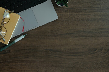 Wall Mural - Flat lay wooden desk with laptop, notebook, glasses, and a small potted plant, for work or study themes.