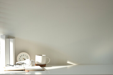 Wall Mural - Minimalistic workspace featuring a white desk with books, a coffee mug, glasses, headphones, and a clock.