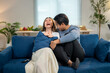 © Wasana - A man and a woman are sitting on a blue couch, laughing and hugging each other