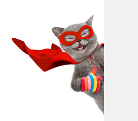 Fototapete - Happy cat wearing superhero costume looking above from behind blank white banner and showing thumbs up gesture. Isolated on white background