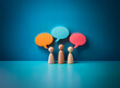 © joeycheung - Three wooden figures stand beneath vibrant speech bubbles against a blue backdrop, symbolizing communication, ideas, and collaborative discussions.