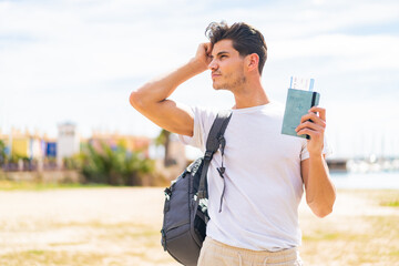 Wall Mural - Young caucasian man holding a passport at outdoors having doubts and with confuse face expression