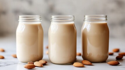 Wall Mural - Three glass jars of almond milk with whole almonds on marble surface