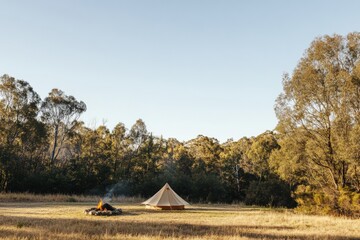 Poster - Camping under clear skies with a cozy fire pit and a canvas tent in a peaceful forest clearing. Generative AI