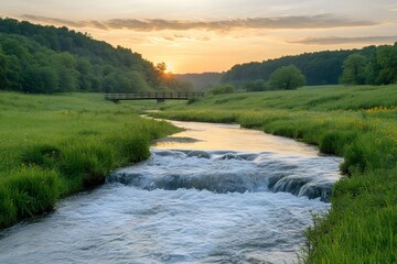 Wall Mural - River flows under wooden bridge at sunset in green meadow