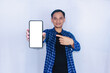 © dailyhomestory.id - Happy Asian man wear casual clothes pointing to the smartphone screen, indonesian man wear blue shirt showing mobile phone blank screen