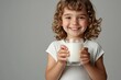 © whitestorm - A radiant little girl with curly hair happily holding a glass of fresh milk, showcasing healthy dental care and nutrition against a light background.