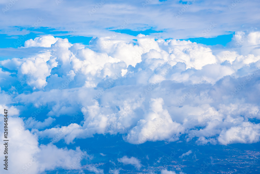 Billowing white clouds fill the bright blue sky over a scenic landscape ...
