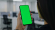 © Nima - Person holding smartphone with green screen in office environment - A woman showcases a smartphone with a green screen in a modern office setting, emphasizing technology, communication, business