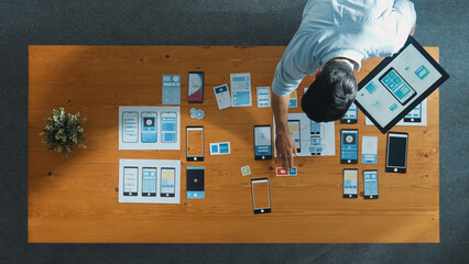 Top down view of software developer holding tablet while choosing icon for mobile phone interface or software program. Start up manager using Ux Ui design to develop wireframe prototype. Convocation.