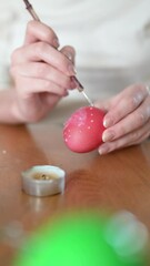 Wall Mural - Young girl dyeing Easter eggs at home. Children painting colorful eggs for Easter hunt. Kids getting ready for Easter celebration. Family traditions. Slow motion vertical close-up footage.