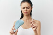 © SHOTPRIME STUDIO - Woman examining hair loss with a hairbrush, displaying concern and frustration against a light grey background Natural lighting highlights the strands of hair on the brush
