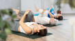 © JackF - Active fit women lying on back in row on mats and performing stretching exercises for lower back while training together in yoga center