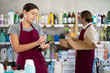 © JackF - Focused young female household goods store worker using tablet to manage inventory of cleaning supplies and toiletries, while male colleague organizing products on shelves in background