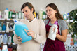 © JackF - Focused middle-aged man carefully examining blue detergent bottle while friendly young female sales assistant offering another product in cleaning supply store