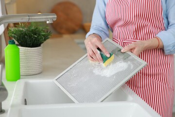 Wall Mural - Woman cleaning filter of kitchen hood with sponge above sink indoors, closeup