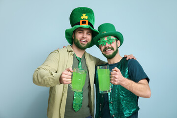 Wall Mural - Young men in leprechaun hats with green beards holding glasses of beer on blue background. St. Patrick's Day celebration