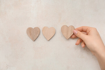 Wall Mural - Female hand with wooden hearts on beige grunge background. Valentine's Day celebration