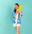 © sitthiphong - Songkran festival in Thailand, Full body length happy smiling young Asian woman in summer wearing floral shirt with plastic glasses and holding water guns in blue background.