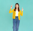 © sitthiphong - Happy smiling young Asian woman casual yellow shirt and standing with points to the upwards with her hand, isolated on blue background.