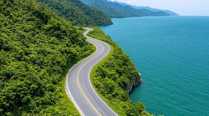 Wall Mural - Travel Road Trips concept. Winding road along a lush green coastline beside a tranquil blue sea under a clear sky.