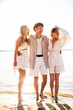 © halayalex - Group of young smiling friends having fun at the seaside. Man and two cute female at sunset in casual summer clothes. Young women hugging his friend at sunrise. Enjoy their life, relax