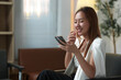 © crizzystudio - Asian businesswoman is sitting on a comfortable chair in her modern office, holding a smartphone and smiling while reading a message or browsing social media