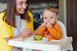 © Westend61 - Happy mother with son eating broccoli sitting on high chair at home
