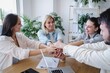 © Westend61 - Smiling creative business people stacking hands at office