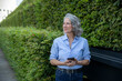 © Westend61 - Businesswoman with smartphone standing by beech hedge in green city