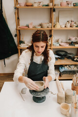 Poster - Craftswoman carefully molds a clay bowl on the potters wheel. Creating ceramic crockery in the workshop.