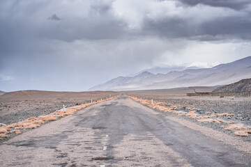 Wall Mural - Asphalt road of the Pamir Highway in the valley of the Tien Shan Mountains in Tajikistan in the Pamirs, landscape in the high desert mountains for background, the road goes into the distance