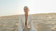 © www.freund-foto.de - Frau in Wüste, Elegante Frau im weißen Blazer sitzt in Wüstenlandschaft. Modernes Fashion-Shooting mit minimalistischer Ästhetik und natürlichem Licht