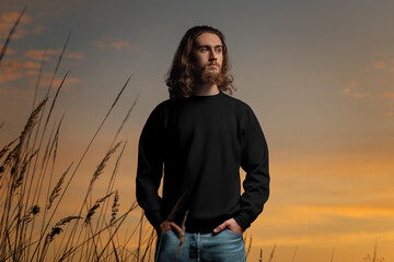 Wall Mural - Mockup of a black sweatshirt on a bearded guy with long hair, outdoors, against a sky background, front view.