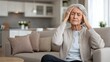 © pvl0707 - An elderly woman is feeling discomfort as she sits on a comfortable sofa in a warm, inviting living room during the daytime