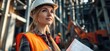 © Design By Reiga - Female engineer reviewing blueprints at construction site. Background shows heavy machinery.  Use Industry stock photo