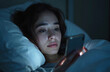 © Vadym - Woman lies in bed at night using smartphone. Sleepless brunette scrolls social media. Mobile phone addiction, insomnia concept. Girl chatting, browsing, reading, texting alone in dark room.