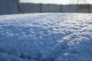 Wall Mural - Glittering snow on a surface with a blurred fence in the background, winter texture