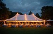 © Vadym - Outdoor wedding reception under illuminated tent at night. Tables adorned with flowers, candles for dining. Elegant event venue surrounded by dark trees on lawn. Romantic atmosphere for celebration.