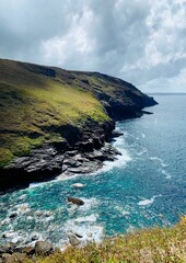 Wall Mural - Cliff view with lush greenery and blue ocean under a partly cloudy sky. Tintagel, Cornwall.