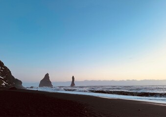 Wall Mural - Scenic view of Reynisfjara's black sand beach with sea stacks under a clear blue sky in Iceland.