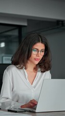 30s middle eastern woman using computer data technology app for work online. Young professional IT specialist latin hispanic business lady working on laptop pc at desk in modern office space. Vertical