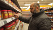 © Bonsales - Man selecting a jar of cooking sauce from a well organized supermarket shelf, carefully reading the label and considering various options