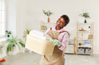 © Studio Romantic - Young happy african american woman housewife holding laundry clothes in basket standing in the living room at home and looking cheerful at camera. Routine washing and housekeeping work concept.
