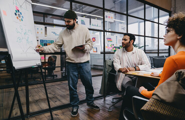 Wall Mural - Focused colleagues analyzing diagrams on board while working on project in office