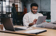 © BullRun - Focused ethnic man working on tablet while sitting at table with laptop