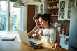 © Marko Geber - Happy couple holding positive pregnancy test looking at laptop