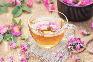 Wall Mural - Dog rose floral  tea in a glass cup with fresh and dry flowers on wooden background, closeup, spring floral drink, natural medicine and naturopathy concept