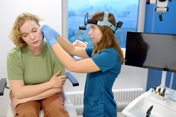 A patient is seen by an otolaryngologist. A professional ENT doctor examines a patient. An otolaryngologist examines a patient's inner ear using an otoscope