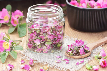 Wall Mural - Dog rose floral dry tea in a wooden spoon with fresh flowers on wooden background, closeup, spring floral drink, natural medicine and naturopathy concept